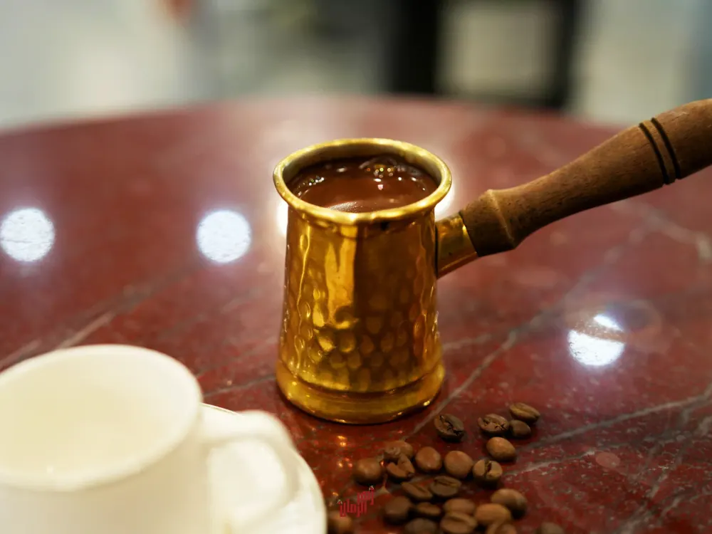 A brass pot of Arabic coffee beside a white cup